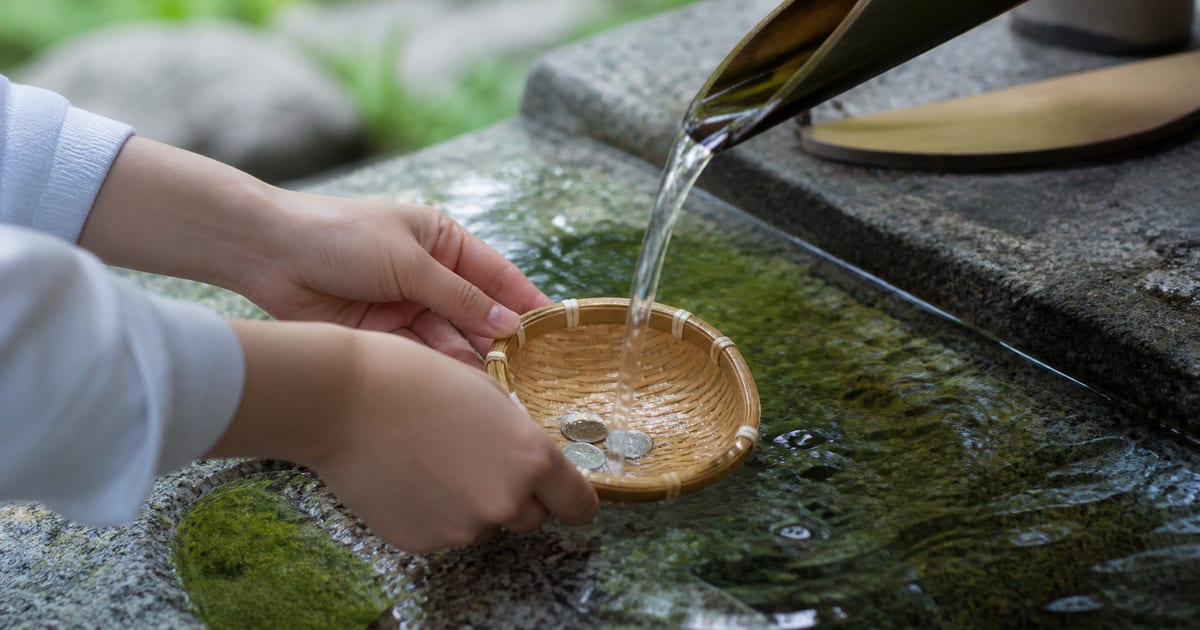 湧水で硬貨を洗う手元とざる